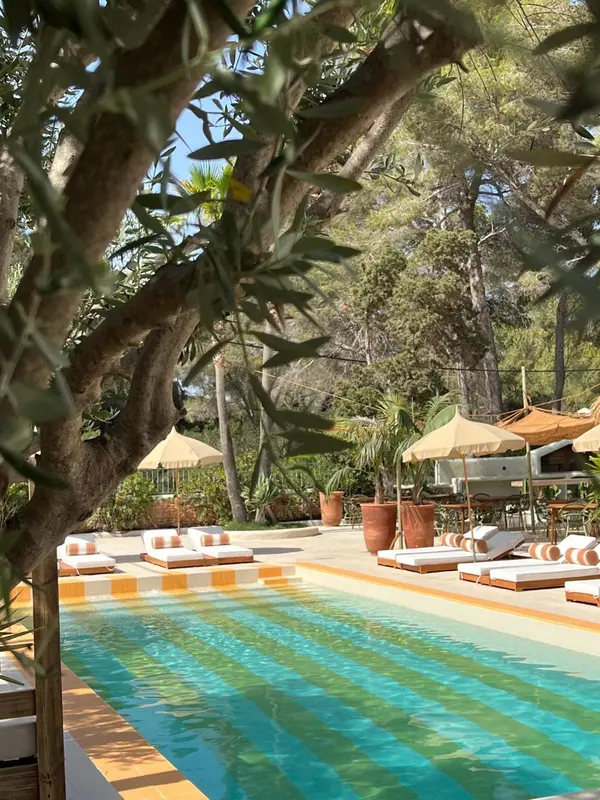 Une piscine turquoise bordée de chaises longues se trouve dans un jardin luxuriant.