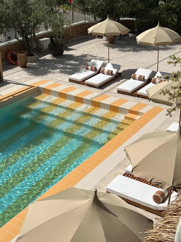 Transats et parasols bordent une piscine carree aux motifs colorés.
