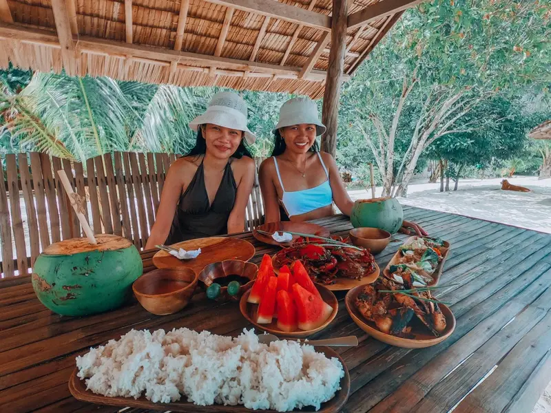Deux femmes sourient devant une table garnie de plats et de fruits.