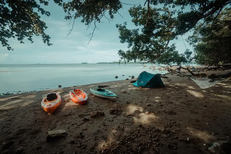 Plage de sable avec des kayaks et des hamacs face à la mer.