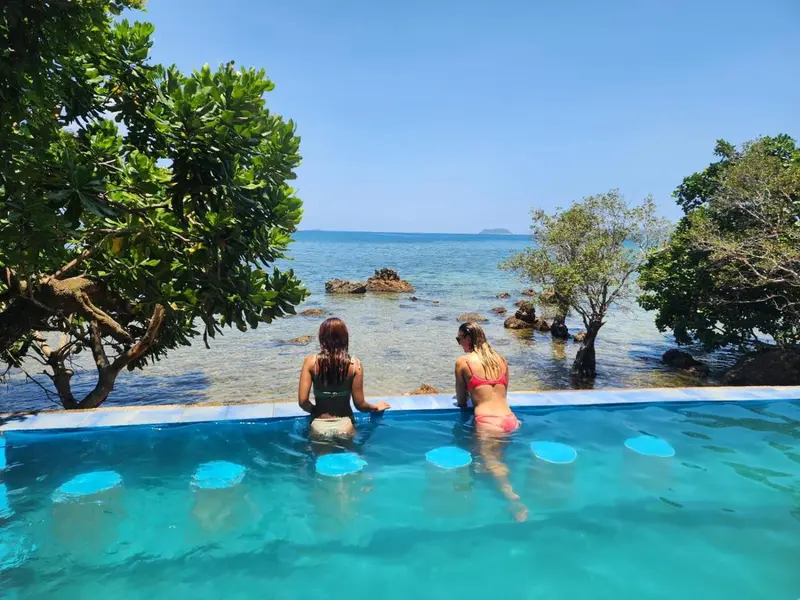 Deux femmes sont assises au bord d'une piscine à débordement face à la mer.