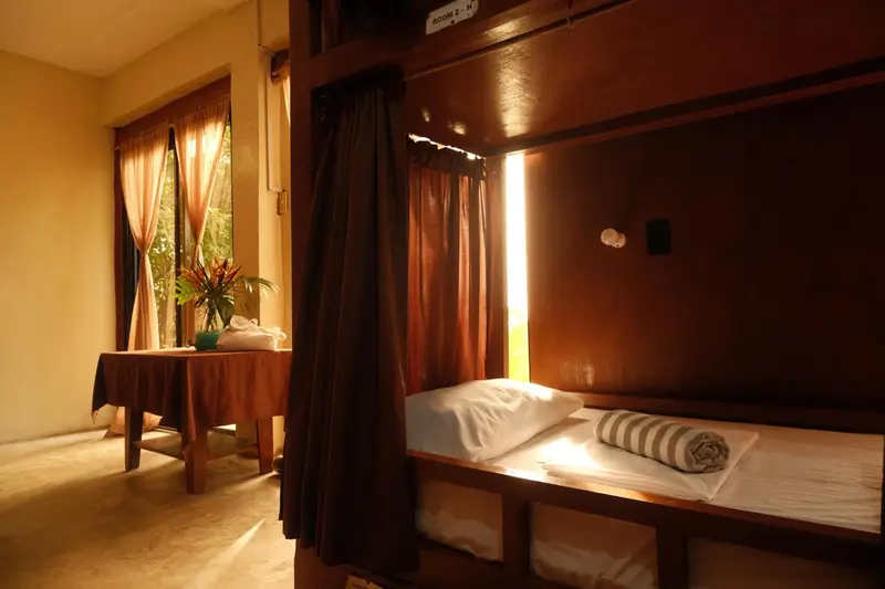 Lit superposé dans une chambre aux rideaux bruns et à la lumière chaude.