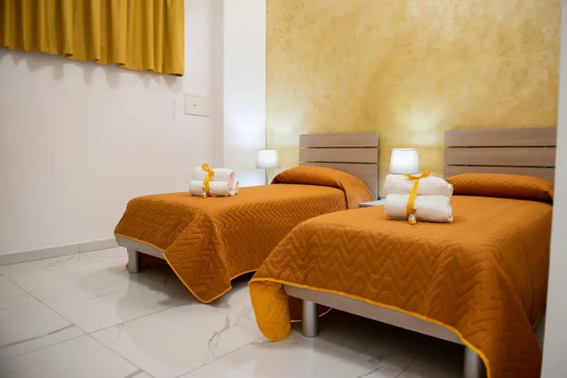 Deux lits simples avec couvertures orange dans une chambre lumineuse.