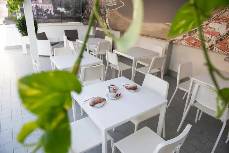 Une table est dressée avec une tasse de café et une viennoiserie sur une terrasse carrelée.