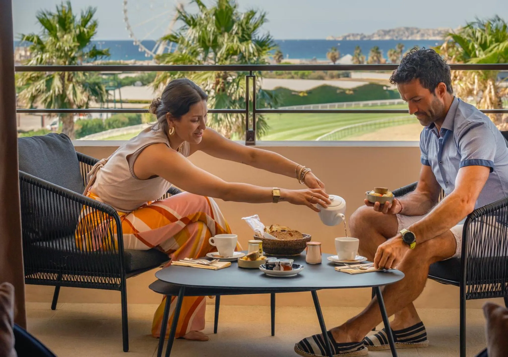 Un couple prend le petit-déjeuner sur une terrasse ensoleillée avec vue sur la mer.