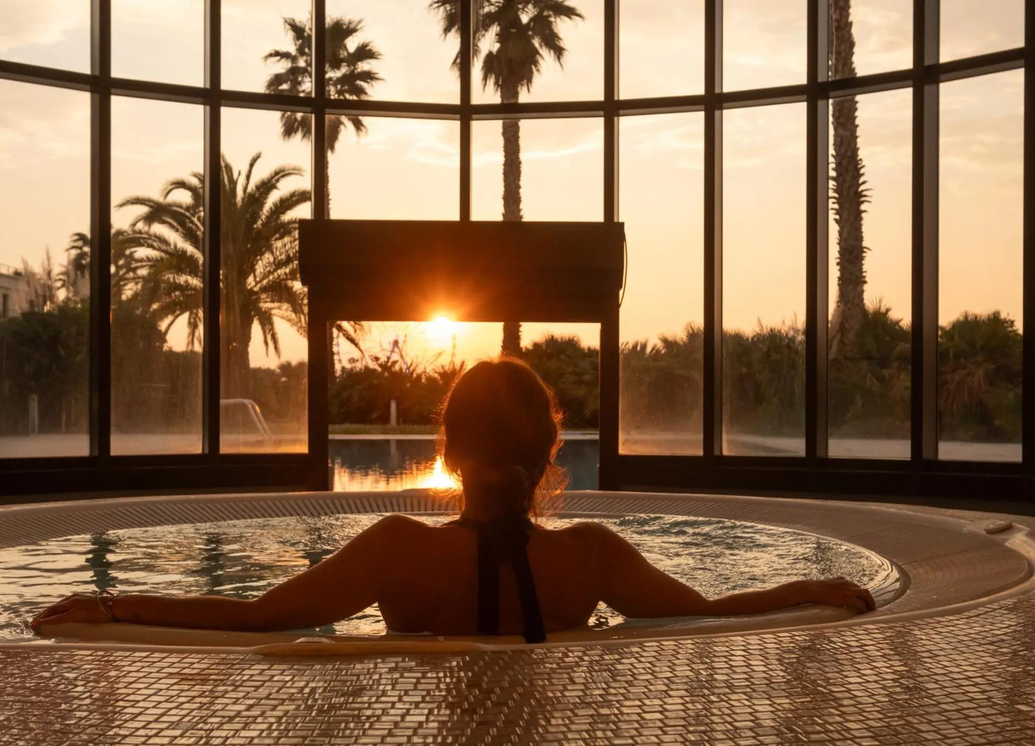 Une personne se détend dans un jacuzzi face à un coucher de soleil tropical.