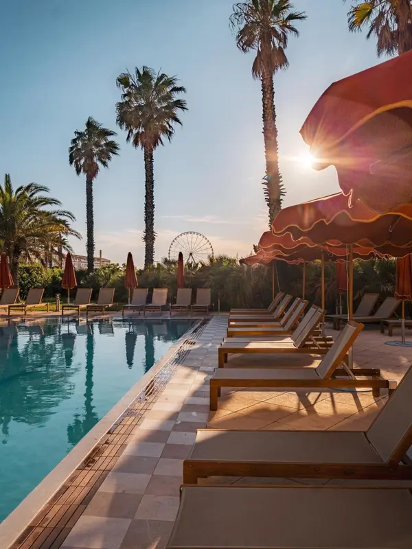 Transats alignés au bord d'une piscine ensoleillée, avec des palmiers en arrière-plan.