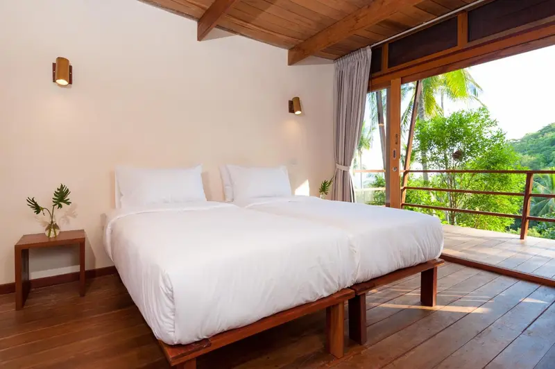 Une chambre lumineuse avec un lit double donnant sur une végétation luxuriante.