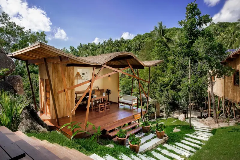 Une terrasse en bois devant un bungalow sur pilotis, entouré de végétation tropicale.