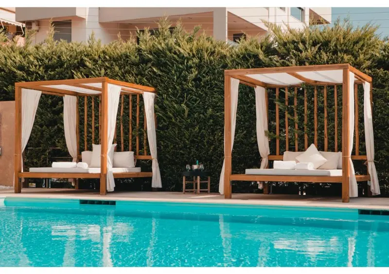 Transats blancs sous des pergolas en bois au bord d'une piscine turquoise.