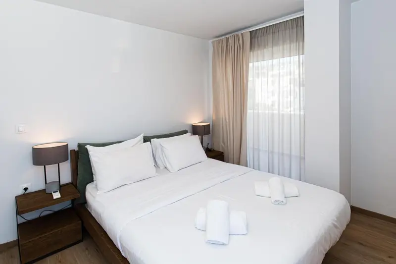 Une chambre lumineuse avec un grand lit recouvert d'une courtepointe blanche et de coussins verts.