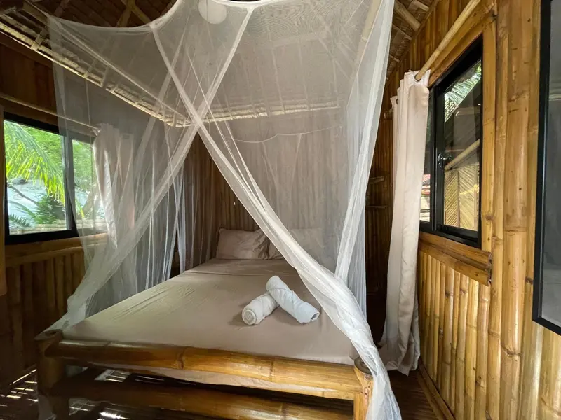 Un lit recouvert d'une moustiquaire dans une chambre en bambou.