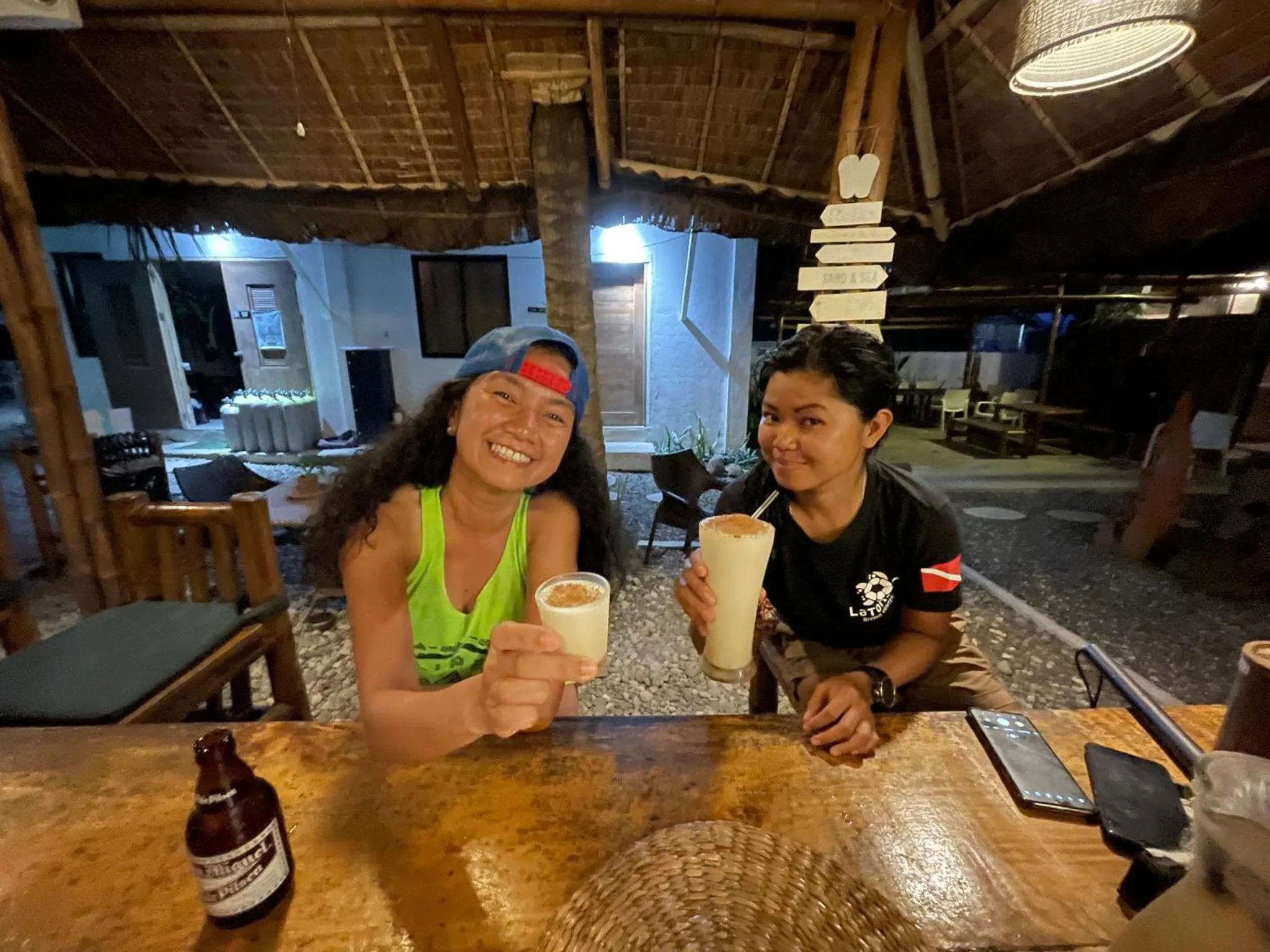 Deux femmes sourient en tenant des verres sur un comptoir en bois.