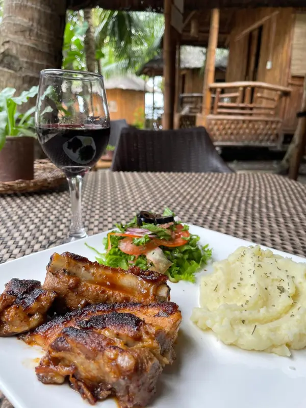 Une assiette de viande grillée accompagnée d'une salade et de purée de pommes de terre est présentée sur une table en extérieur.