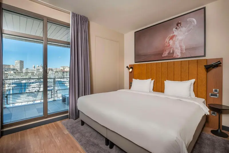 Chambre lumineuse avec un grand lit et une vue sur le port.