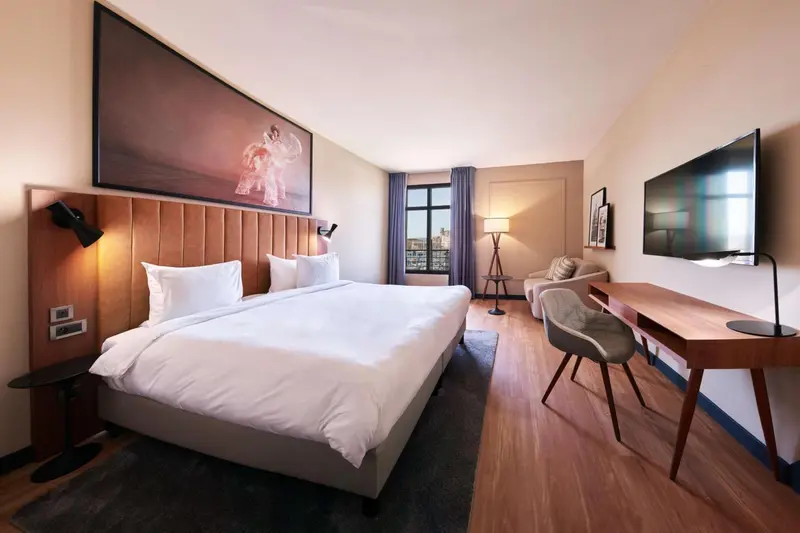 Chambre lumineuse avec un grand lit et un espace bureau.