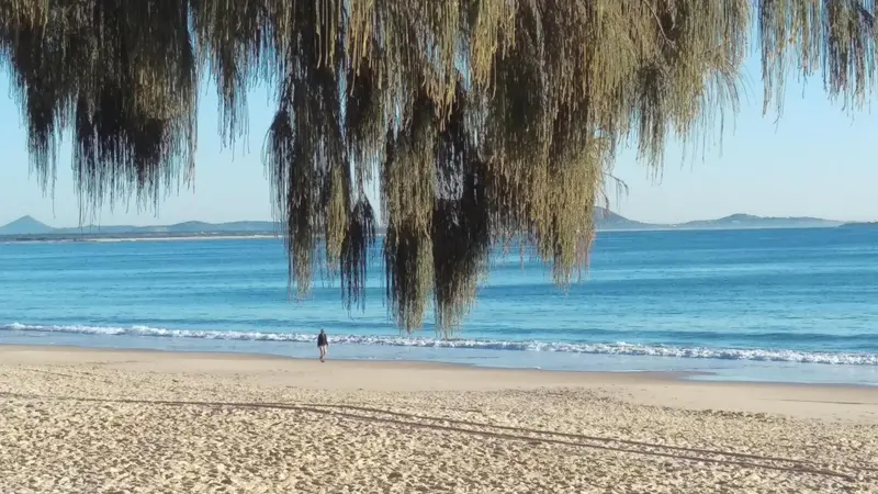 Une plage de sable fin bordée d'une mer turquoise sous un ciel bleu.