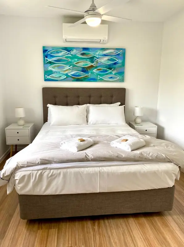 Une chambre lumineuse avec un grand lit recouvert d'une courtepointe blanche et de coussins.