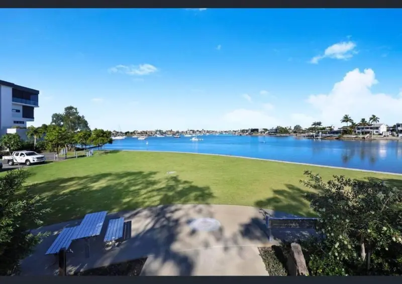 Vue d'un parc verdoyant au bord de l'eau avec des bancs et des arbres.