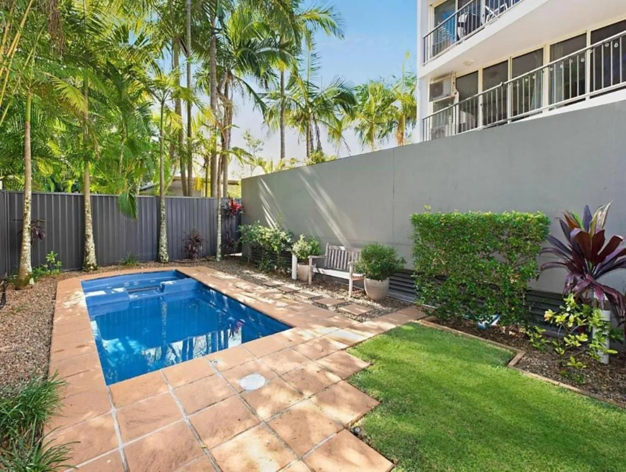 Petite piscine rectangulaire entourée d'une terrasse et d'une végétation luxuriante.