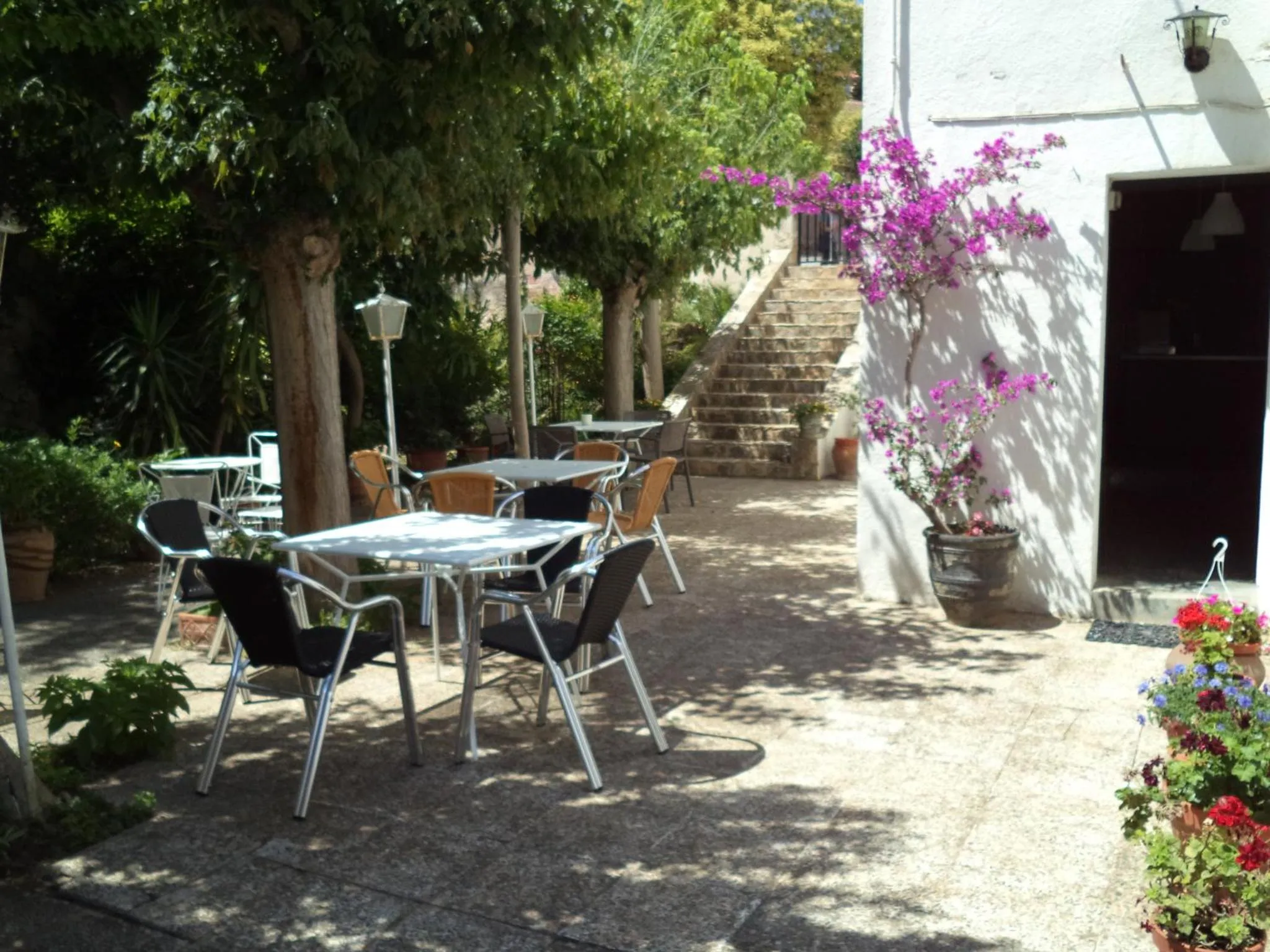 Terrasse ombragée avec tables et chaises près d'un escalier.