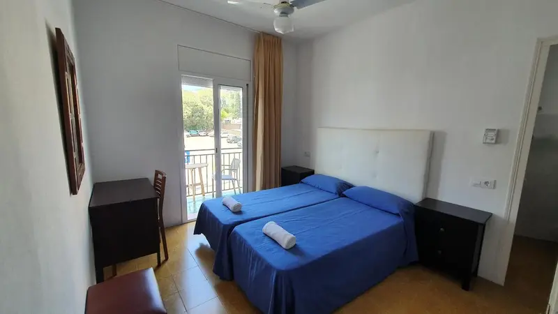 Une chambre lumineuse avec deux lits simples et un accès à un balcon.