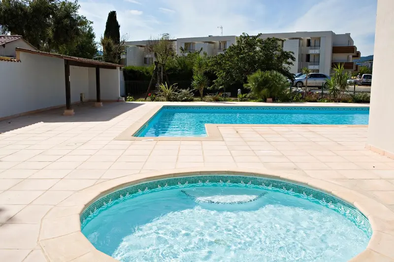 Piscine rectangulaire et jacuzzi extérieur entourés d'une terrasse carrelée.