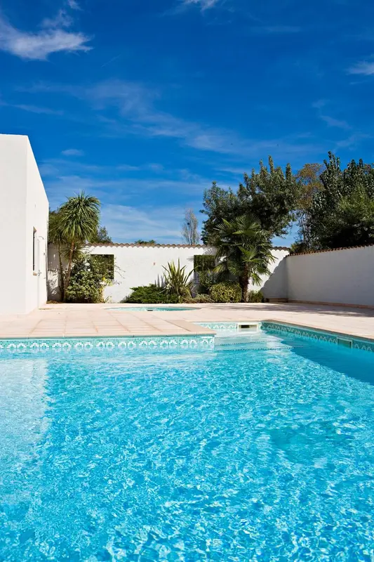 Une piscine turquoise reflète le ciel bleu, bordée d'une terrasse carrelée et de végétation luxuriante.