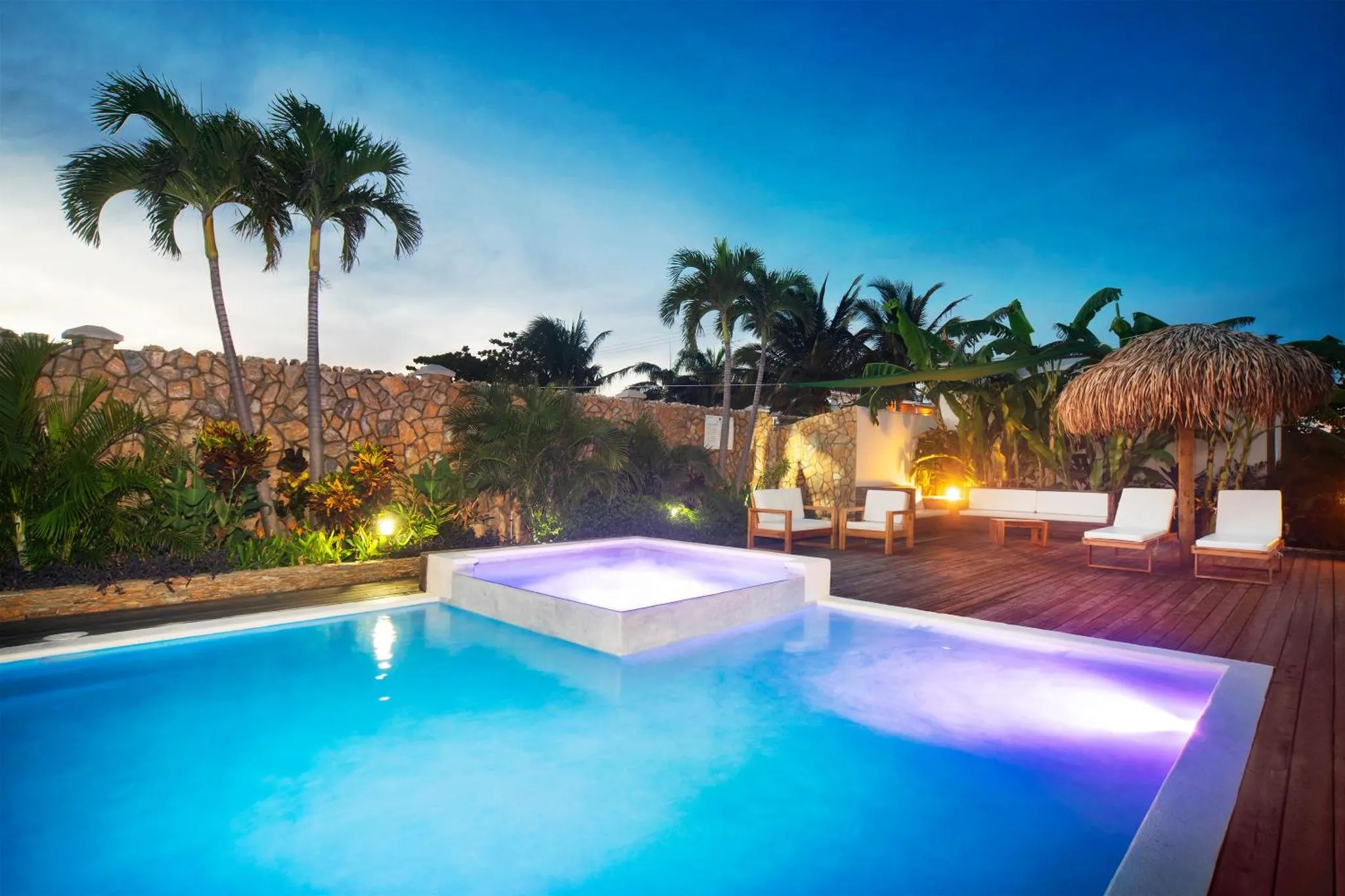 Une piscine illuminée au crépuscule, avec des transats et des palmiers en arrière-plan.