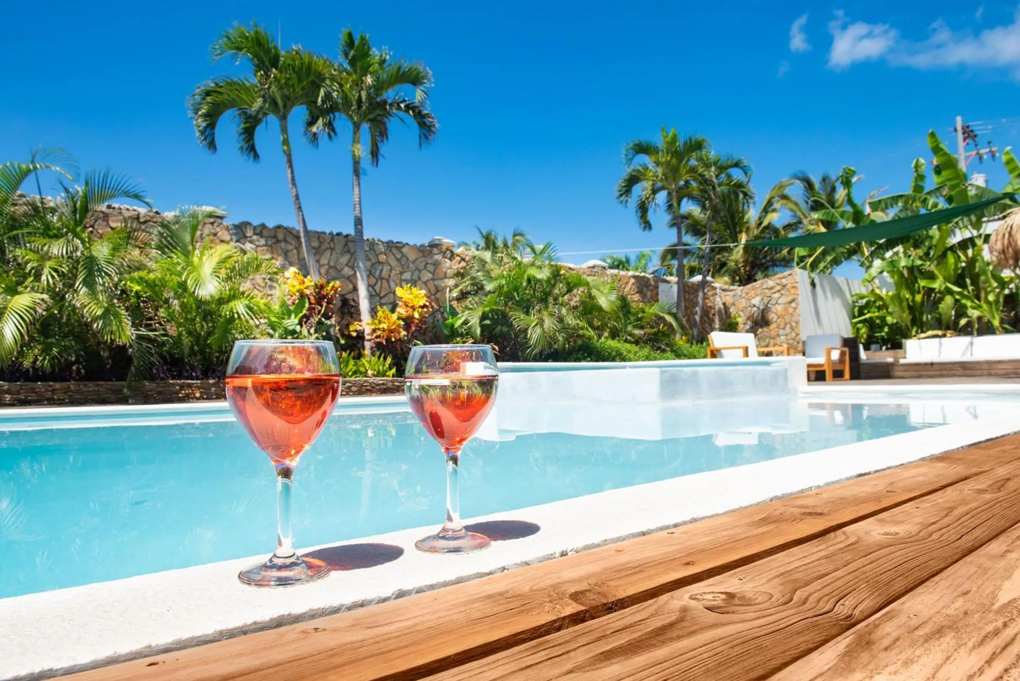 Deux verres de boisson colorée reposent sur le bord d'une piscine ensoleillée.