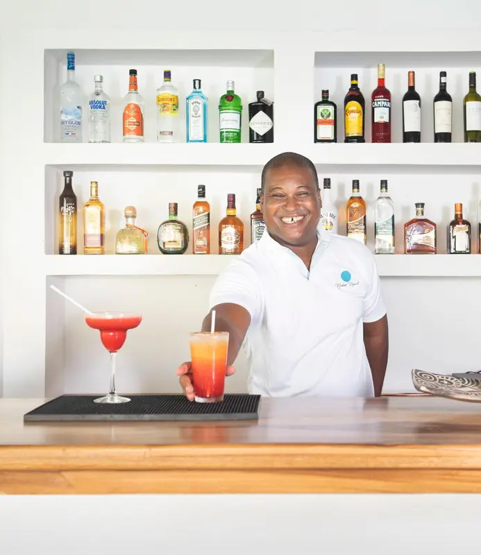 Un barman souriant sert des cocktails devant une étagère remplie de bouteilles.