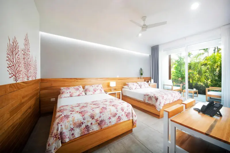 Chambre lumineuse avec deux lits et vue sur une végétation luxuriante.