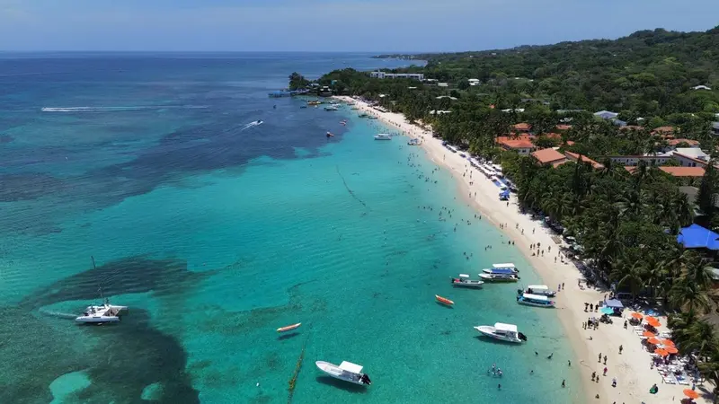 Vue aérienne d'une plage de sable blanc bordée d'une eau turquoise et d'une végétation luxuriante.