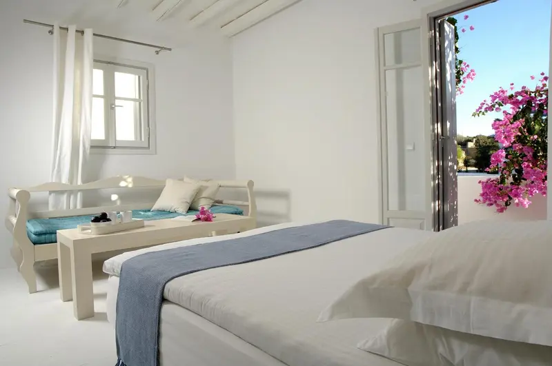 Une chambre lumineuse avec un lit et un coin salon donnant sur une terrasse fleurie.