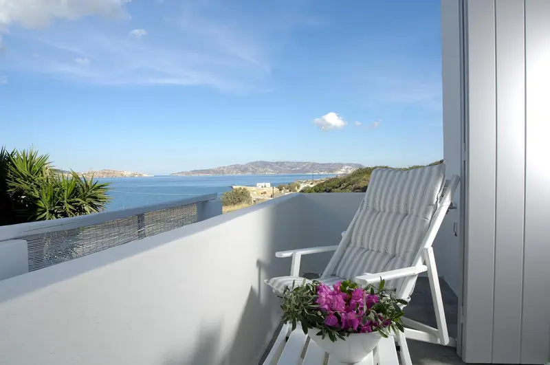 Une chaise longue sur une terrasse ensoleillée offre une vue sur la mer et les collines.