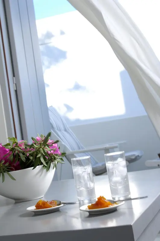 Une table avec des verres d'eau et des fruits frais près d'une fenêtre ouverte sur la mer.