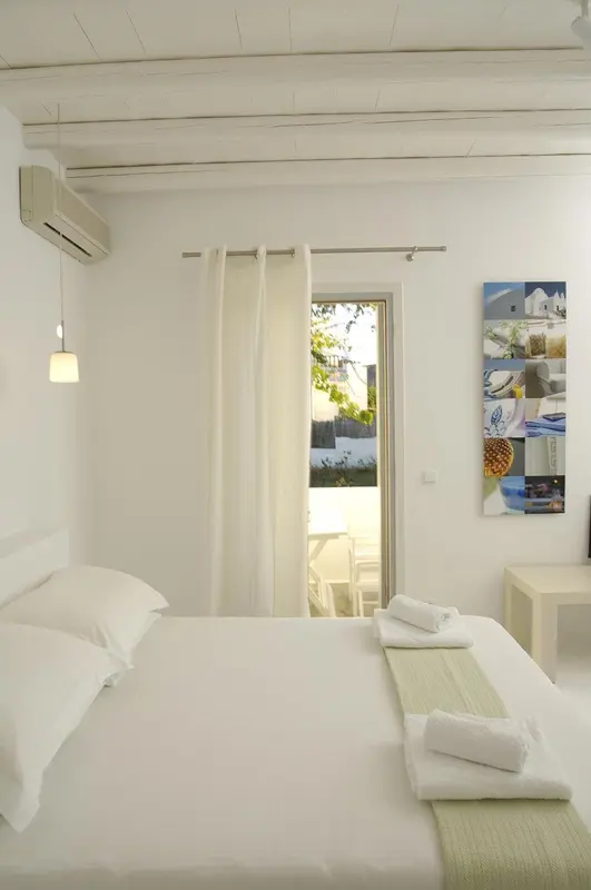 Une chambre lumineuse avec un lit recouvert de linge blanc et une porte-fenêtre ouverte sur une vue extérieure.