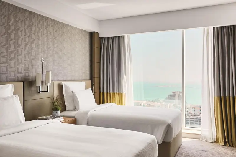 Chambre lumineuse avec deux lits simples et vue sur la mer.