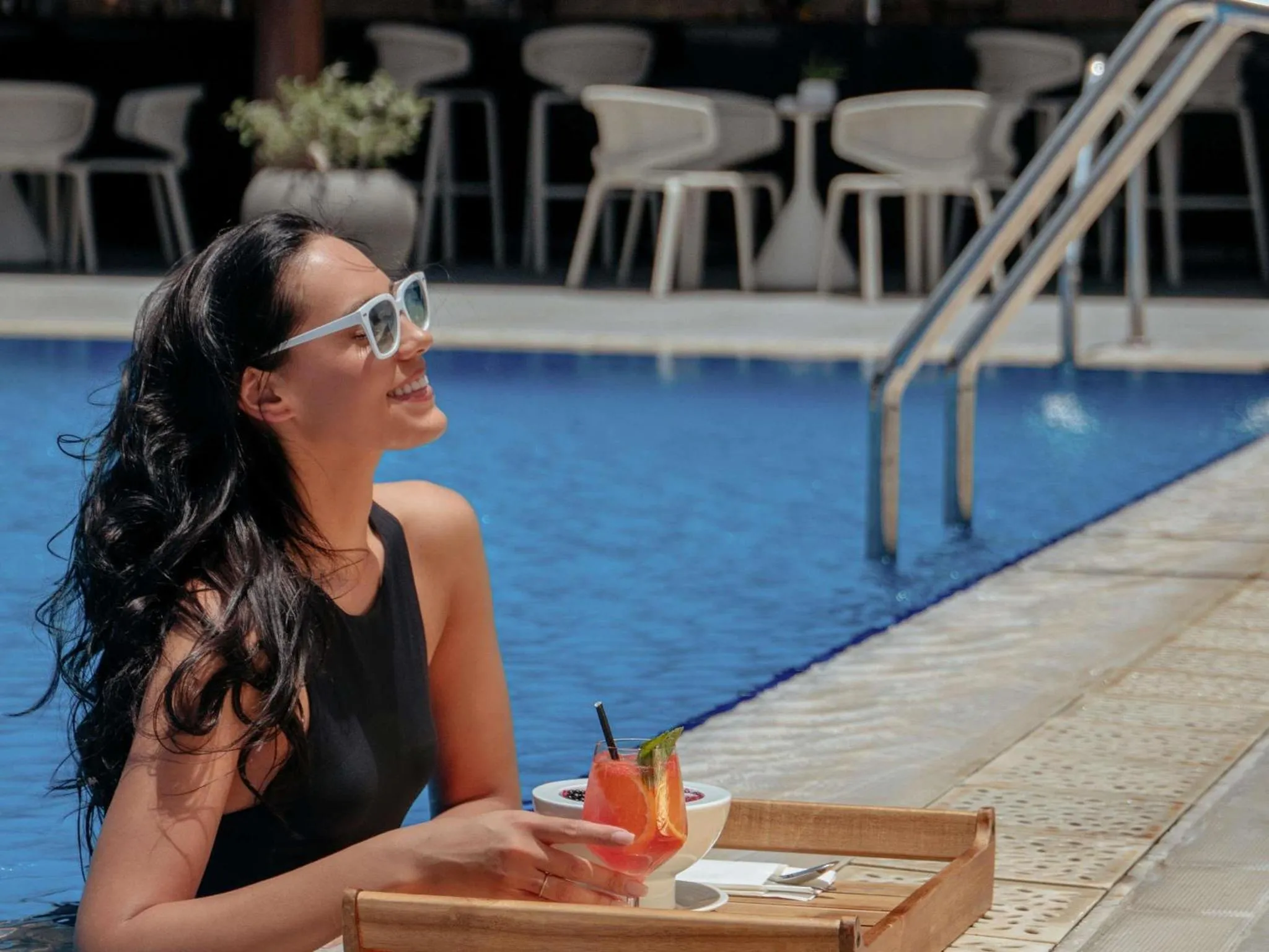 Une femme souriante se détend au bord d'une piscine avec un cocktail.