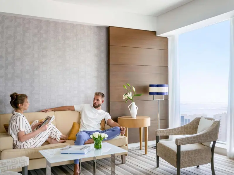 Un couple est assis sur un canapé dans un salon lumineux avec vue sur la mer.