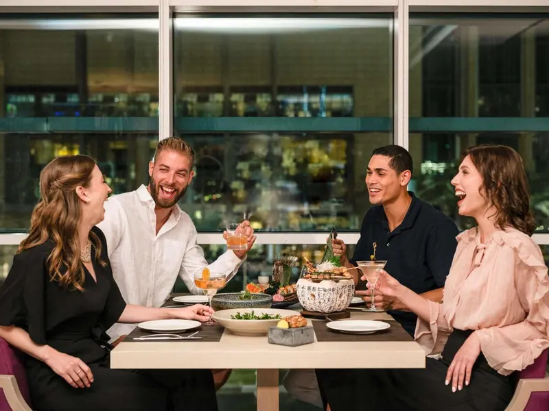 Quatre personnes sont assises autour d'une table, partageant un repas et des boissons.