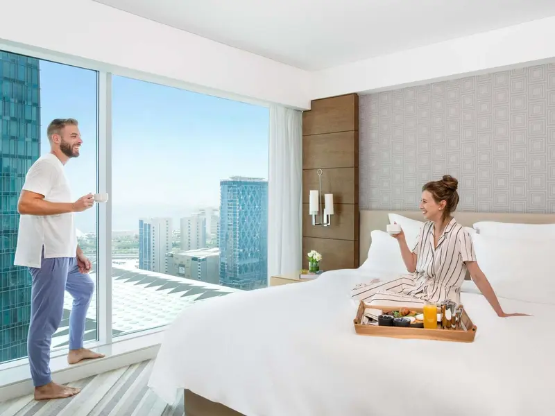 Un couple prend son petit-déjeuner au lit dans une chambre avec vue sur la ville.
