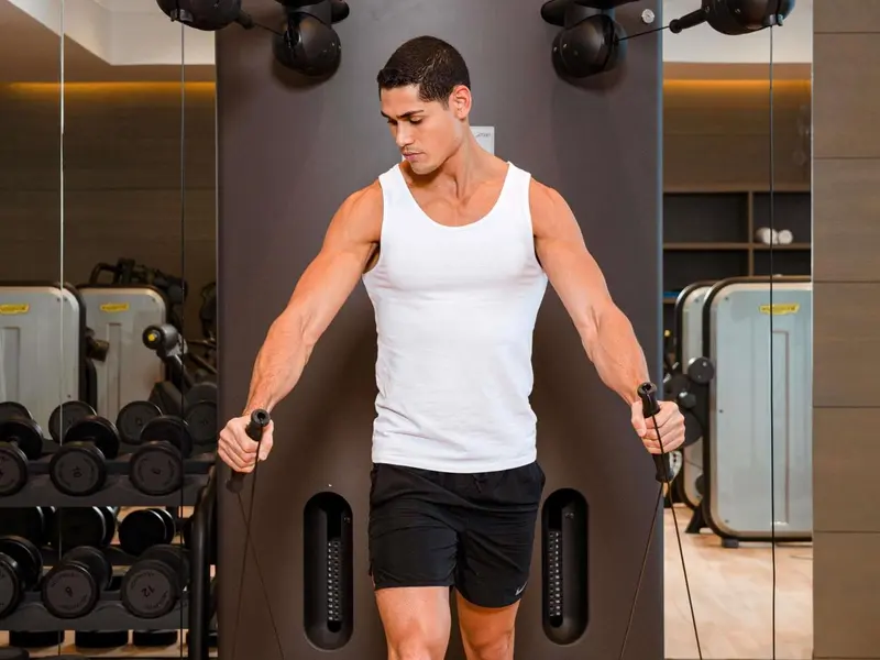 Un homme musclé s'entraîne avec des câbles dans une salle de sport.