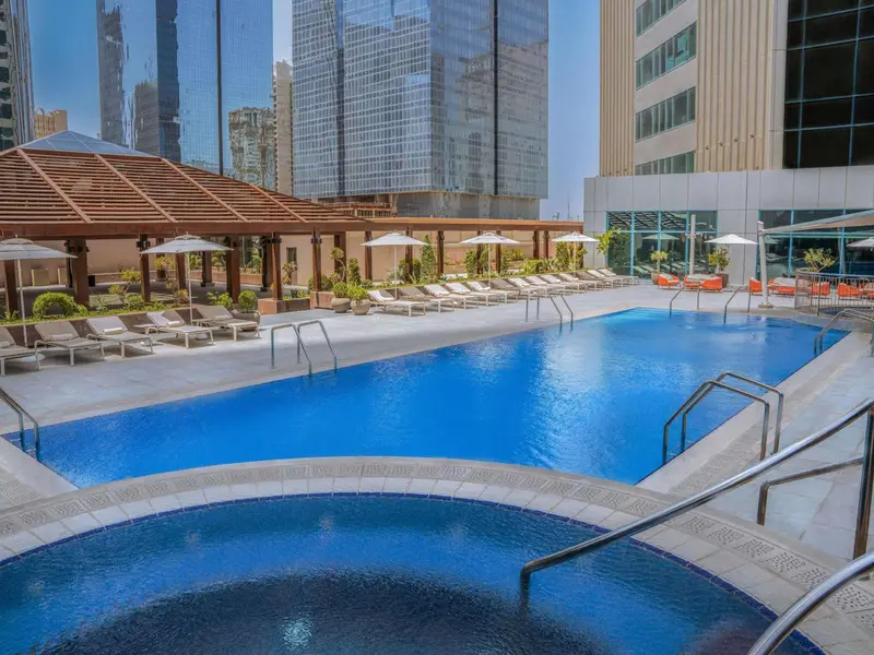 Une piscine rectangulaire avec un espace jacuzzi intégré, entourée de transats et de parasols.