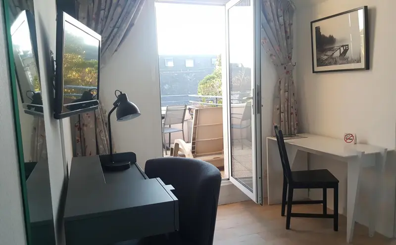 Une chambre lumineuse avec un bureau et un accès à un balcon.