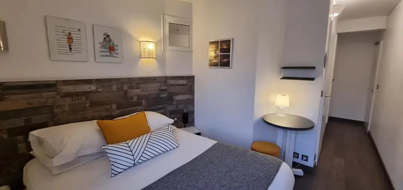 Une chambre lumineuse avec un lit recouvert d'un plaid et d'oreillers colorés.