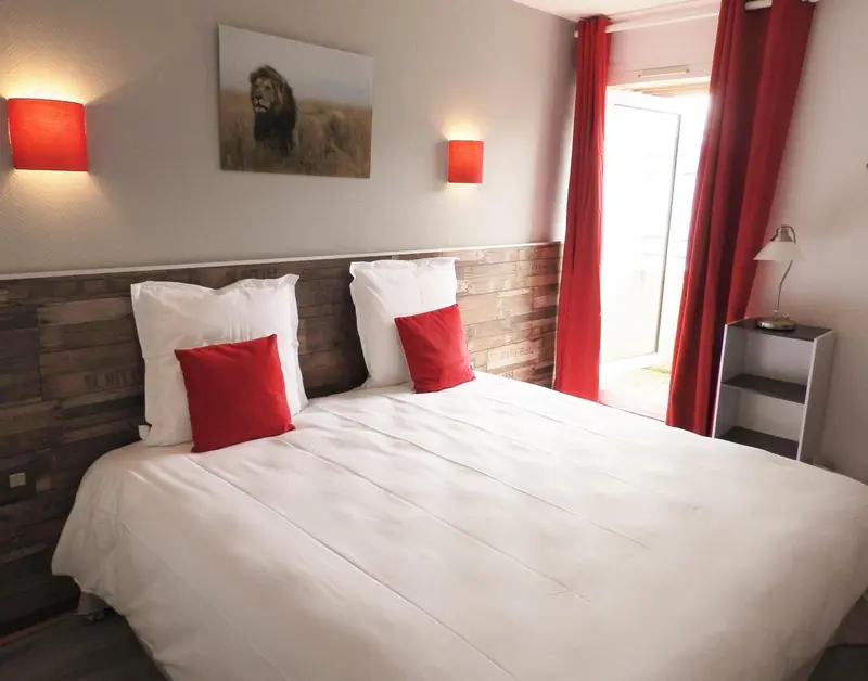Une chambre avec un grand lit recouvert d'une courtepointe blanche et de coussins rouges.