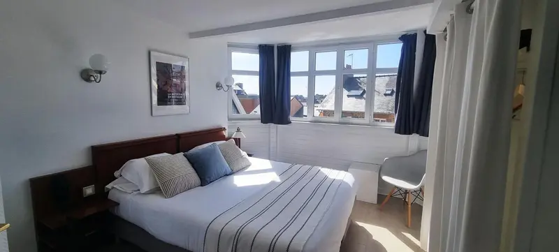 Une chambre lumineuse avec un lit double et une vue sur les toits.