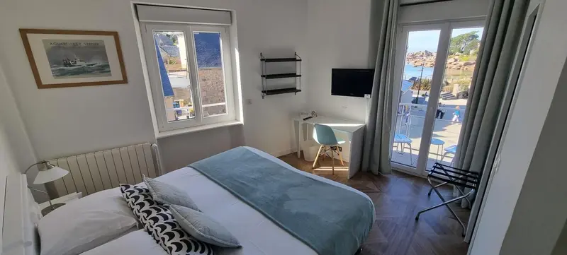 Une chambre lumineuse avec un lit fait et un bureau près d'une fenêtre donnant sur la mer.