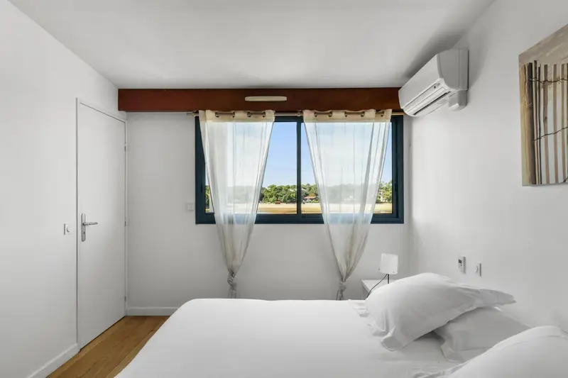 Une chambre lumineuse avec un lit blanc et une fenêtre.